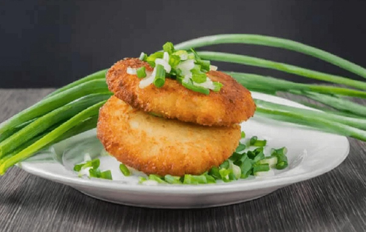 کوکو سیب زمینی با شیر درون یک بشقاب سفید با مقداری پیازچه و خیلی ترد و خوشبو و خوشمزه به نظر می‌آیند